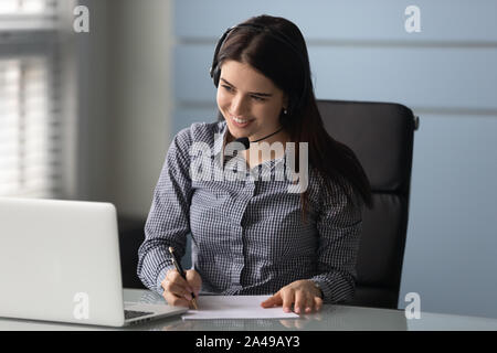 Smiling businesswoman watching educational webinar, writing down notes. Stock Photo
