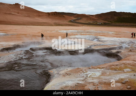 Boiling mudpots in the geothermal area Hverir and cracked ground around with unrecognisable tourists, Iceland in summer. Myvatn region, North part of Stock Photo