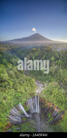 Aerial drone image of Tumpak Sewu waterfall with Mount Semeru volcano erupting in the background in Eastern Java, Indonesia Stock Photo