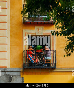 Madrid, Spain - Oct 13, 2019: Middle aged couple enjoying drinks and a chat on a balcony with historic artwork on the facade Stock Photo