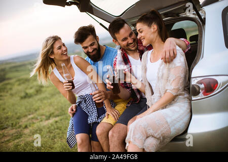 Group of young people sitting in the car trank during trip in the nature Stock Photo