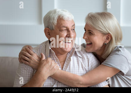 Elderly hoary couple embracing sitting on couch indoors Stock Photo