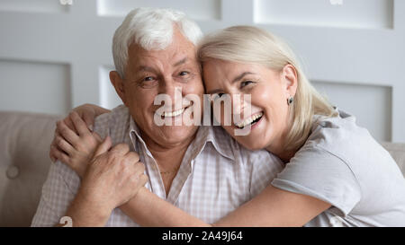 Happy mature couple in love seated on couch embracing Stock Photo