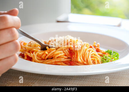 Female hand holds a fork with spaghetti. Breakfast or dinner outdoors, close-up. Stock Photo