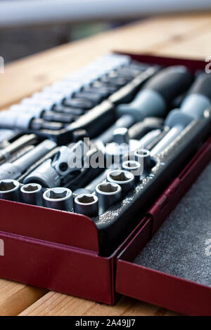 Metallic red box with a set of wrenches lying on a wooden table in natural light. Close-up. Stock Photo