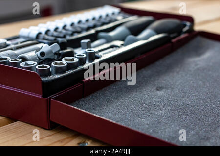 Metallic red box with a set of wrenches lying on a wooden table in natural light. Close-up. Stock Photo