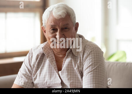 Elderly man seated on couch smiles looking at camera Stock Photo