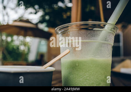 close up view of cool half full plastic mug of green tea smoothie with straw Stock Photo