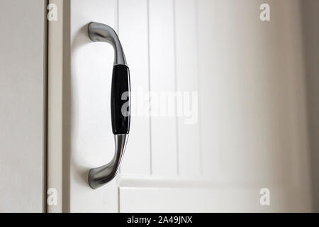 Handle on white painted kitchen cabinet door in soft light. Close-up. Stock Photo