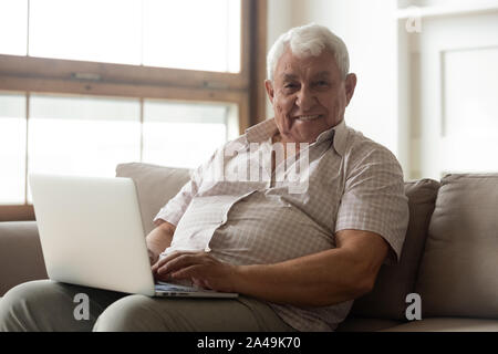 80s man seated on couch with laptop looking at camera Stock Photo