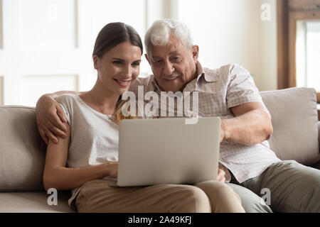 Grandfather and adult granddaughter sitting on couch using laptop Stock Photo