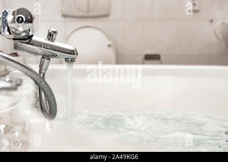 Clean water flows from a chrome mixer to a luxurious spa bath, with air bubbles to relax. Bathroom with WC. Stock Photo