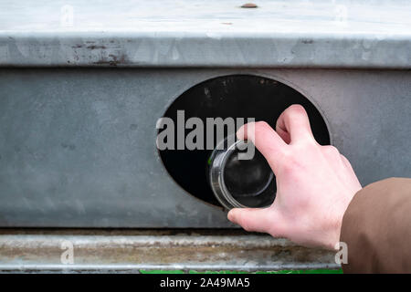 Human hand throws used white cans of canned baby food into a container for recycling. Waste sorting. The concept of respect for the environment. Close Stock Photo