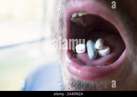 Tablets of several colors, sizes and shapes on the tongue, in the mouth are ready to eat, on prescription. Close-up. Stock Photo