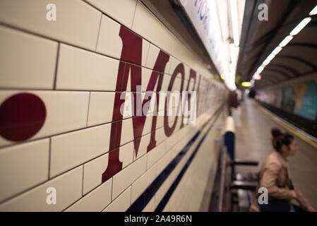 London, United Kingdom - September 15, 2019: A woman waits for the tube under the ecru tiles and sign of Mornington Crescent, an Underground Station. Stock Photo