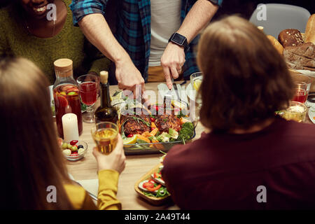 Close up of unrecognizable people enjoying dinner together, focus on man cutting delicious meat loaf set on wooden table, copy space Stock Photo