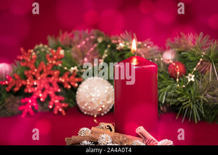 fir branch with golden star necklace and baubles in the background. burning red candle with cinnamon sticks in the foreground. Light bokeh Stock Photo