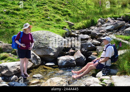 Walkers cooling feet in water in a beck, Cumbria Stock Photo