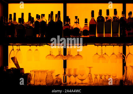 Bottles and glasses sitting on shelf in a bar, back lit, brand names removed Stock Photo