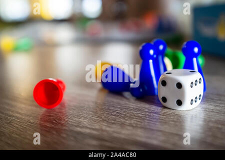Dice and multi-colored plastic chips from a children's board game, lie on a wooden table in natural light, on a blurred background. Close-up. Stock Photo