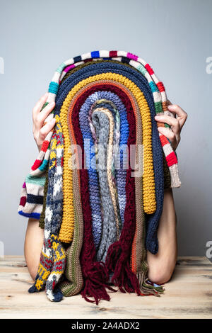 Girl is fooling around in the winter while waiting for the summer and jokingly made a funny mask of multicolored scarves in the shape of rastaman face Stock Photo