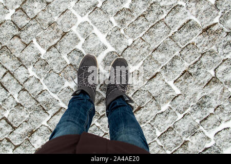 Women's legs in stylish suede boots stand on the snow-covered pavement of granite cobblestones, on a winter cold day. Stock Photo
