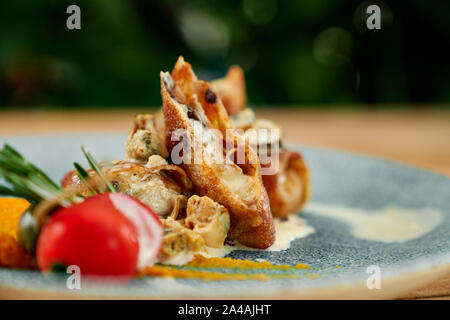 Tasty pancakes with mushrooms and cheese, served on blue plate with white sauce and tomato. Stock Photo