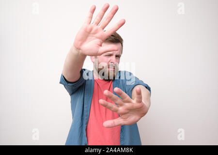 A calm, confident man put his palms forward as protection and narrowed one eye. Isolated on white background. Close-up. Stock Photo