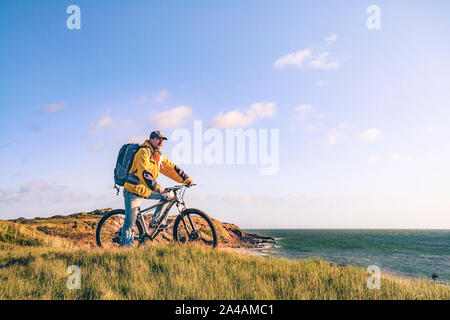 Cycling Ireland. Recreational cyclist with mountain bike and backpack on the edge of the sand dunes looking at the sea.