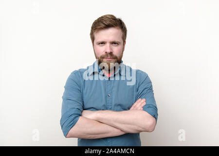 A contented bearded man stands confidently with his arms folded and stares intently. Isolated on white background. Close-up. Stock Photo