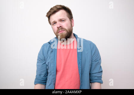 A weary, tortured young man who has a headache looks sadly with narrowed eyes. Isolated on white background. Close-up. Stock Photo