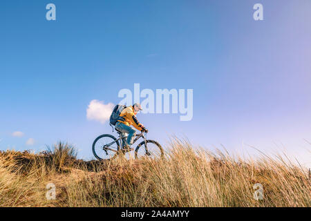 Cycling Ireland. Recreational cyclist with mountain bike and backpack riding downhill in sand dunes.