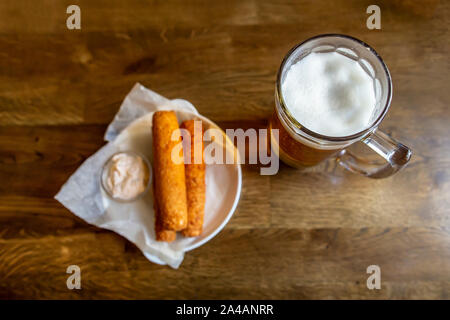 Mug of cold lager beer, on a blurred background, a snack of fried crispy cheese with a sauce, on a wooden table, in a pub. View from above. Close-up. Stock Photo