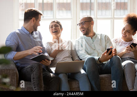 Happy diverse friends laughing at funny joke, using electronic devices Stock Photo