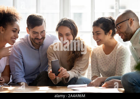 Smiling diverse friends using mobile phone, looking at screen Stock Photo