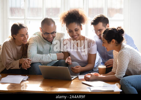Happy diverse friends using laptop together, looking at screen Stock Photo