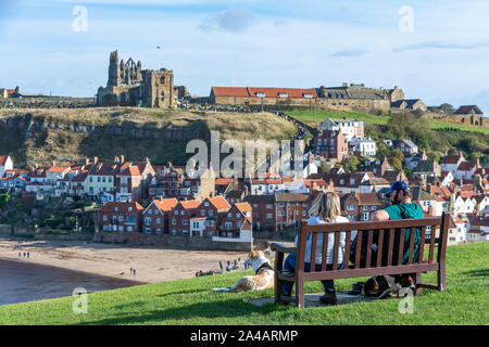 Man and woman with anxious dog overlooking the East Cliff beach below Whitby Abbey and The Church of Saint Mary