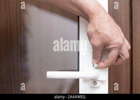 A man is holding a metal screw with which he is going to fasten a handle on a PVC window. Close-up. Stock Photo