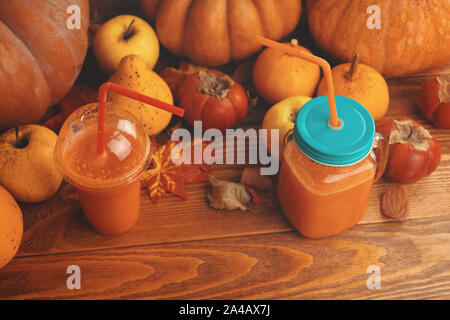 Pumpkins juice in bottles with pumpkins. Two glasses cups of pumpkin juice, pumpkins and fallen ma. Ple leaves on kitchen table Stock Photo