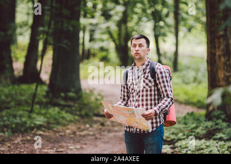Man with Backpack and map searching directions in wilderness area. Tourist with backpack using map in forest. concept tourism holidays. Hiking man Stock Photo