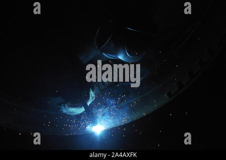 Professional welder welds an industrial tank in a workshop. Stock Photo