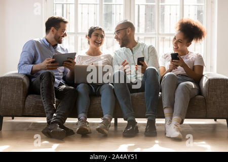 Happy diverse friends using devices, having fun, discussing news Stock Photo