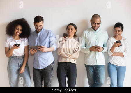 Smiling diverse people using phones, standing in row near wall Stock Photo