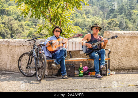 7-15 2019 Tbilisi Georgia - Two street musicians sit on bench at tourist spot near castle above city playing guitars with  beer between them and a pat Stock Photo