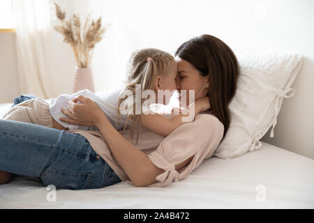Happy mother and little daughter hugging, laying in comfortable bed Stock Photo