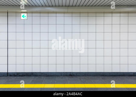 Closeup View of a Regular Public Corridor. Nobody is in the Tunnel with White Square Tiles, Yellow Tactile Paving and Exit Sign. Stock Photo