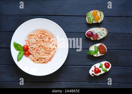Spaghetti and appetizer bruschettas with tomatoes, salmon, creamy cheese, basil, grapes, blue cheese, pear, avocado with cherries tomatoes on black wo Stock Photo