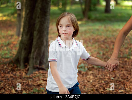 Special kid walking outdoors holding his mother's hand cropped Stock Photo