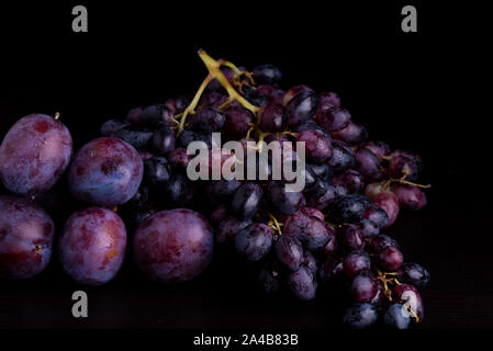 fresh blue plums and grapes on a black reflective background Stock Photo