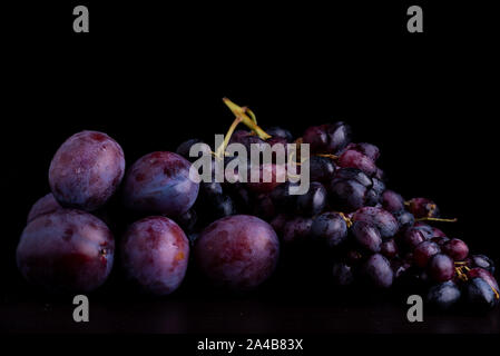 fresh blue plums and grapes on a black reflective background Stock Photo